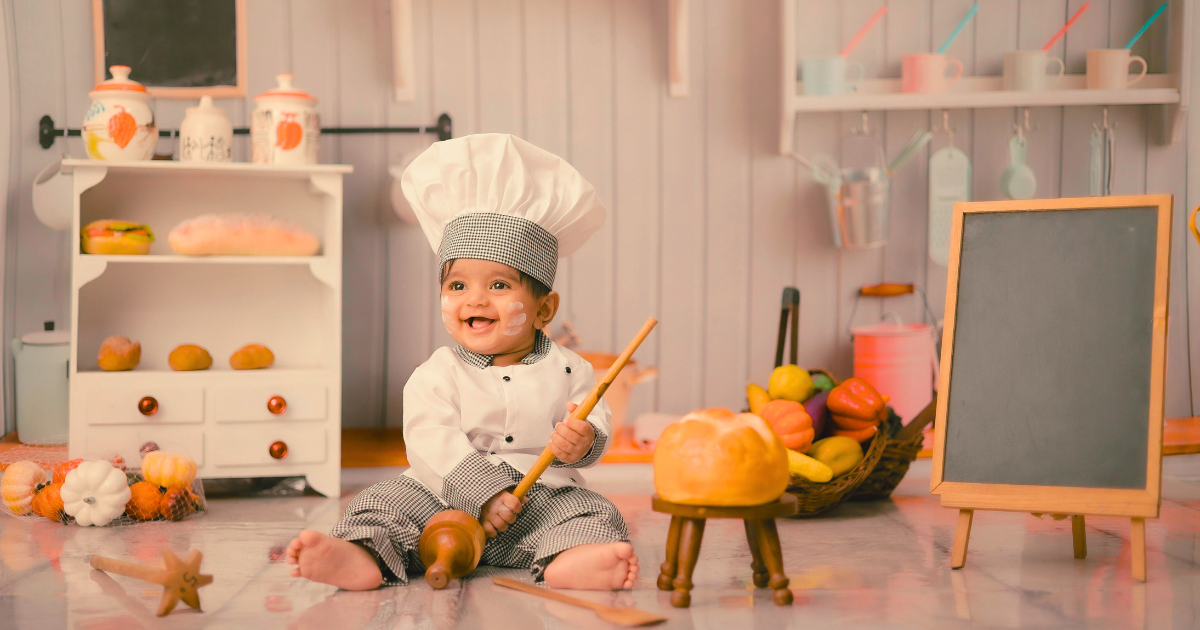 should you buy your toddler a play kitchen - toddler in chef hat sitting among kitchen toys