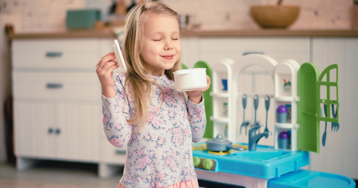 child sniffing pretend soup while happily playing with a realistic play kitchen