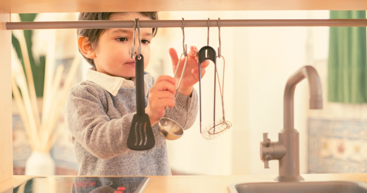 Toddler boy playing with pretend kitchen utensils on play kitchen for toddlers